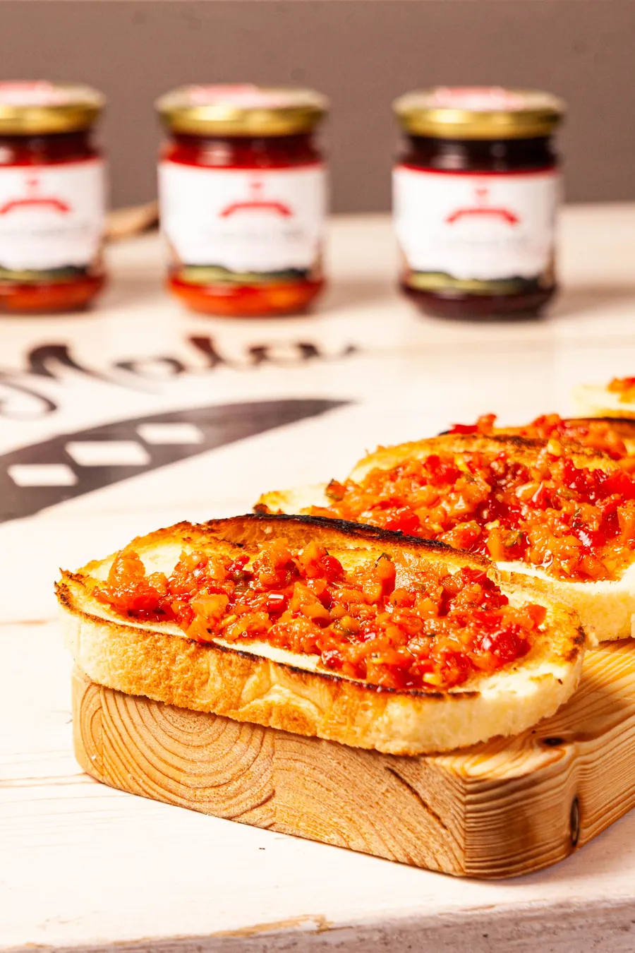 Bruschette condite con la conserva sul tagliere, vasetti sullo sfondo
